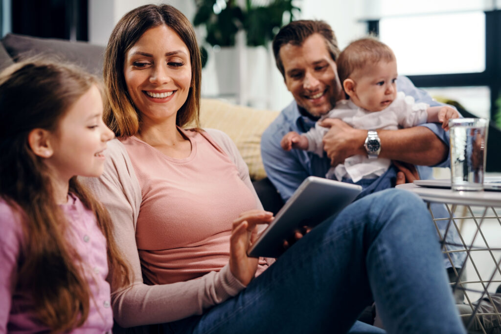 Happy Mother Daughter Using Digital Tablet While Father Is Holding Baby Boy Home 1024x683